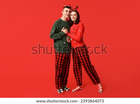 Happy young couple in Christmas pajamas on red background
