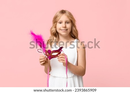 Funny little girl with carnival mask on pink background