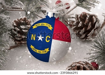 Christmas ball with the flag of North Carolina, decorates the snow tree with snowfall. The concept of the Christmas and New Year holiday