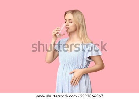 Beautiful young pregnant woman with glass of water on pink background