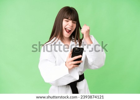 Little Caucasian girl doing karate over isolated background with phone in victory position