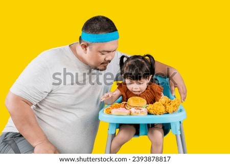 Bad overweight father gives daughter unhealthy junk food on high chair isolated over yellow background