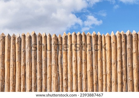 Palisade and cloudy sky as abstract rustic or historical background. Fence made of tightly driven stakes. Royalty-Free Stock Photo #2393887467