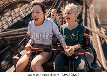 Shot of happy young people riding a roller coaster. Young women and men having fun on amusement park ride.