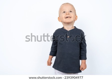 Cute beautiful blond two year old baby boy standing over white studio background and gesturing from happiness, dancing and playing. 
