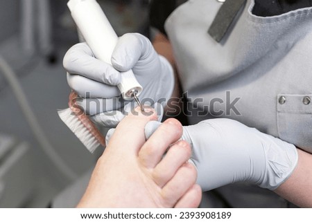 The process of filing off a thickened old nail from the fingers of an elderly woman. Procedure podologist.  Royalty-Free Stock Photo #2393908189