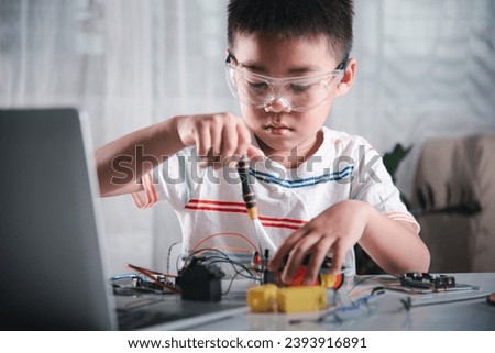 Asian kid boy assembling the Arduino robot car homework project at home, Little child tighten the nut with a screwdriver to assemble car toy, creating electronic AI technology workshop school lesson