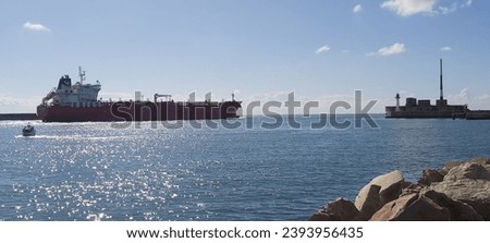 A sailing vessel is pictured on a tranquil body of water against a backdrop of dramatic rocks and a majestic building