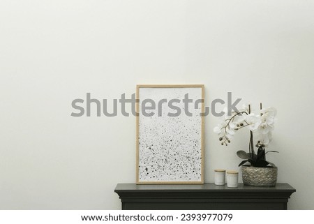Picture frame, candles and orchid on fireplace near white wall indoors, space for text. Interior element