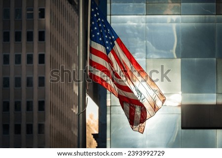 American flag waving in the wind on the pole in front of large windows and buildings of Lower Manhattan, New York City