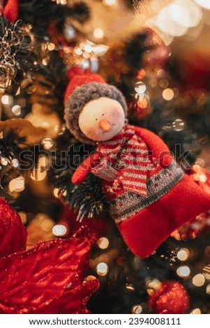 Soft toy snowman figurine hanging on a Christmas tree with golden garland lights.