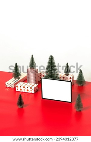 Christmas concept flat lay with gift boxes and Christmas trees. White  blank screen digital tablet mockup on red background. 