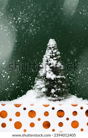 Christmas tree and a Christmas gift wrapped with shiny paper under snow. 