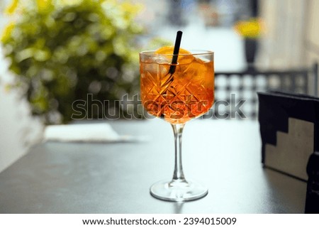 Aperol Spritz Cocktail. Alcoholic beverage based on table with ice cubes and oranges outdoors. Served cocktail with orange slice and straw placed on the table of sidewalk cafe in Italy
