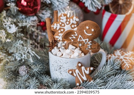Homemade Christmas ginger cookies in powdered sugar. Delicious gingerbread man in a mug with coffee and marshmallows on the background of a bokeh of Christmas tree lights.