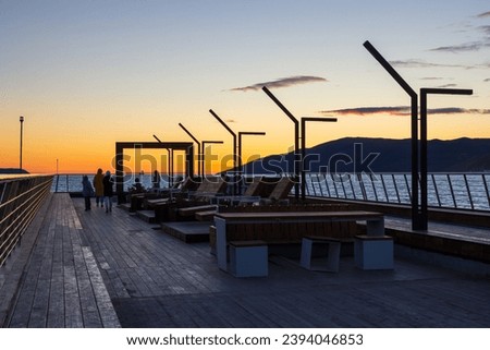 Recreation area on the pleasure pier in Nagaev bay. Beautiful sunset. Benches and sun loungers for relaxation. Travel and tourism in Siberia and the Russian Far East. Magadan, Magadan region, Russia. Royalty-Free Stock Photo #2394046853