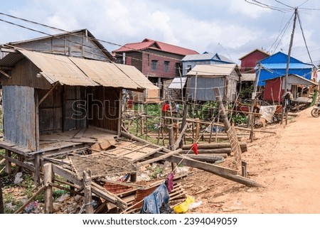 Houses made from corrugated iron on wooden stilts in Kampong Phluk Floating Village, a village with a lot of poverty, with a dirt track road in Cambodia. Royalty-Free Stock Photo #2394049059