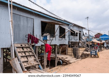 Houses made from corrugated iron on wooden stilts in Kampong Phluk Floating Village, a village with a lot of poverty, with a dirt track road in Cambodia. Royalty-Free Stock Photo #2394049067