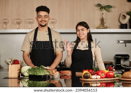 Waist up shot of smiling young middle eastern man and happy hispanic woman looking at camera while posing by kitchen counter