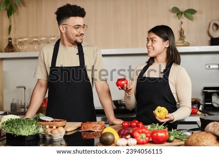 Young middle eastern guy and happy hispanic girl with vegetables in her hands looking at each other while posing at kitchen