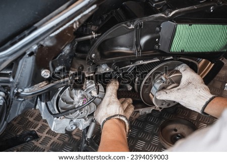 Mechanic check the condition of motorcycle or big scooter drive belt .Check the belt tension at motorcycle garage.Motorcycle belt drive maintenance Royalty-Free Stock Photo #2394059003