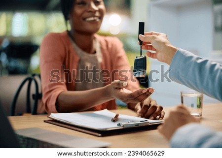 Close up of car sales person giving African American woman key of her new car in showroom. Royalty-Free Stock Photo #2394065629