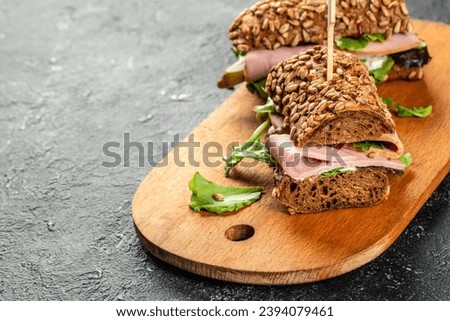 Two delicious ham sandwiches with pickled cucumbers served on a wooden board.
