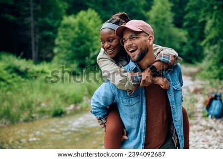 Young playful couple of hikers piggybacking in nature. Copy space. Royalty-Free Stock Photo #2394092687