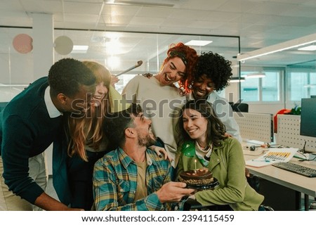 A diverse businesspeople is celebrating a birthday at the office. A man is holding a birthday cake and making a wish while multicultural colleagues singing a birthday song and having a party.