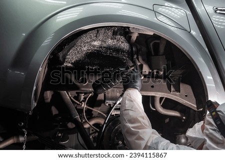 The master sprays an anti-corrosion compound on the bottom of the car. Royalty-Free Stock Photo #2394115867