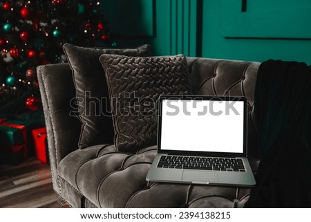 Laptop with blank screen on a desktop and Christmas tree with lights in the background.