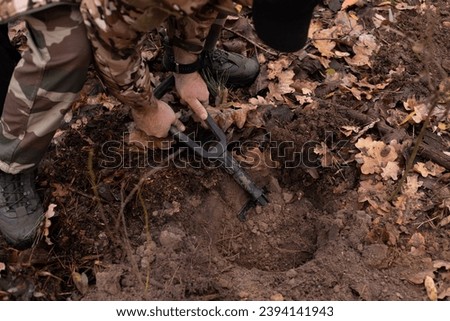a man in military uniform digging a hole in the woods with a sapper shovel Royalty-Free Stock Photo #2394141943
