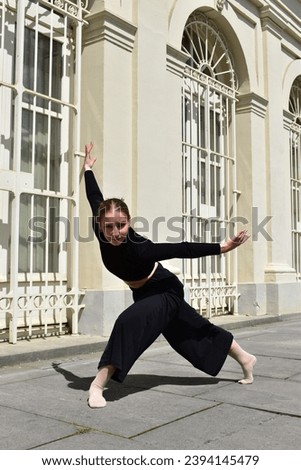 Young woman in black outfit performing a contemporary dance move in front of window with white bars