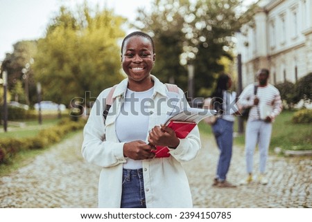Shot of a young woman carrying her schoolbooks outside at college. Beautiful young woman with backpack and books outdoors. College student carrying lots of books in college campus.