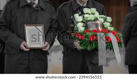 Metal urn or funeral container with ash of a deceased person at a memorial service. Undertakers seen carrying the picture and an urn on a last path towards the grave