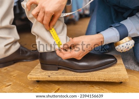 Measuring trouser length with tape on man's ankle above brown shoe Royalty-Free Stock Photo #2394156639
