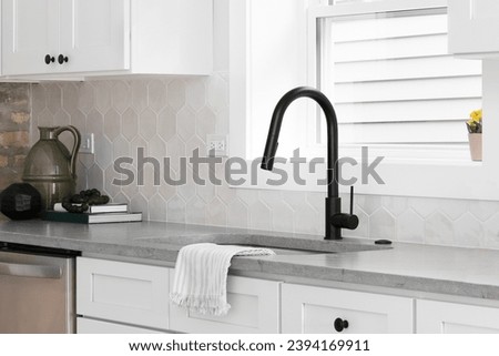 A beautiful kitchen sink detail with white cabinets, marble countertops, and a hexagon tiled backsplash. Royalty-Free Stock Photo #2394169911