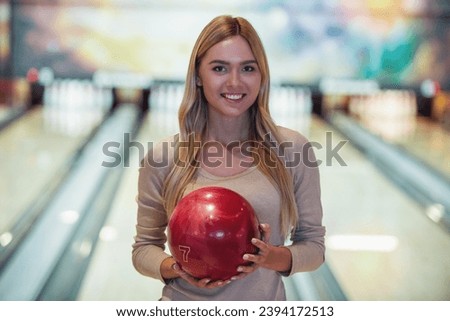 Attractive blonde girl is holding a bowling ball, looking at camera and smiling ready to play bowling