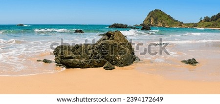 Australian coast with volcanic rocks at the shore on the beach, view from the beach to the sea landscape with blue water and waves on a summer sunny day.