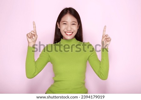 Standing and pointing happily, Portrait of a beautiful young woman in a light pink background, happy and smile, posting in stand position.