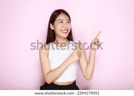 Standing and pointing happily, Portrait of a beautiful young woman in a light pink background, happy and smile, posting in stand position.