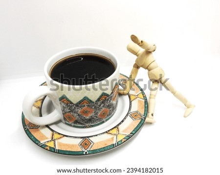 The black coffee in a simple classic patterned cup with a wooden mannequin model that has a "need more coffee" concept photographed on an isolated white background
