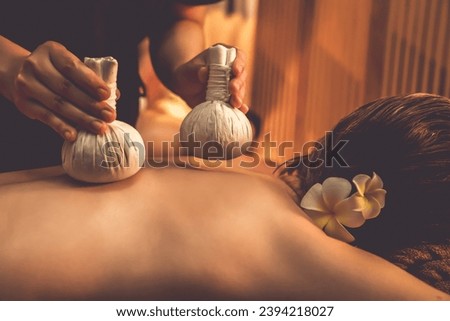 Hot herbal ball spa massage body treatment, masseur gently compresses herb bag on couple customer body. Serenity of aromatherapy recreation in warm lighting of candles at spa salon. Quiescent Royalty-Free Stock Photo #2394218027