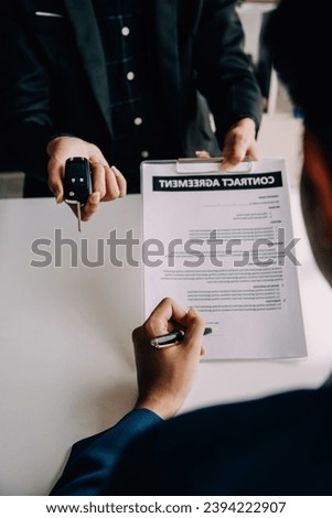 A car rental company employee is handing out the car keys to the renter after discussing the rental details and conditions together with the renter signing a car rental agreement. Concept car rental. Royalty-Free Stock Photo #2394222907