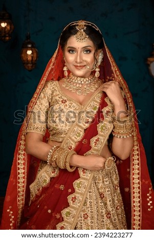Stunning Indian bride dressed in traditional bridal lehenga with heavy gold jewellery and veil posing fashionable in studio lighting. Wedding fashion and lifestyle. Royalty-Free Stock Photo #2394223277