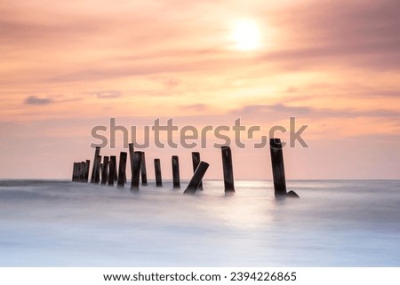 Landscape view of the concrete columns of the old port with Beautiful sky sunrise and strong water waves on Sao Iang Beach at Phetchaburi province. Long exposure picture 
