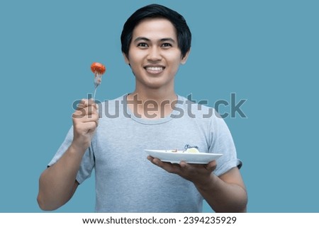 A man in a gray shirt is holding a fork and a plate containing food, for design and visual editing purposes.