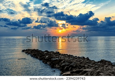 Colorful sunset on the Black Sea. Sea breakwaters. Seascape at sunset under a cloudy sky. Waves on the sea and dark clouds in the blue sky. Sunset over the sea with waves. Royalty-Free Stock Photo #2394239743