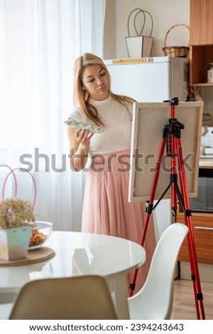 Young woman artist with palette and brush painting abstract pink picture on canvas at home kitchen. Art and creativity concept. High quality photo