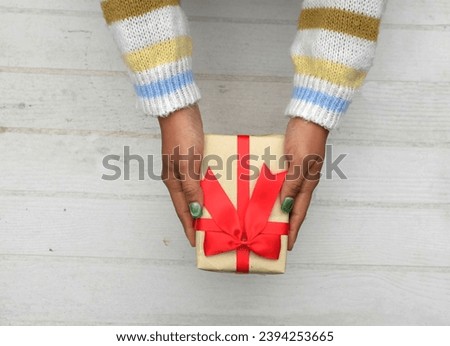 view from above of
girl asian hands in Colorful sweater holding craft paper gift box with red ribbon bow on a white wooden table.
for giving in special day,Christmas, new year,
Valentine
